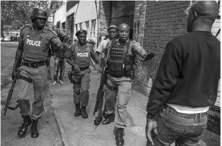 Armed members of the SAPS gesture to a Nigerian man to keep his distance to prevent him from approaching a South African Man who has been arrested while in the process of looting a Nigerian owned business in Jeppestown, Johannesburg. 