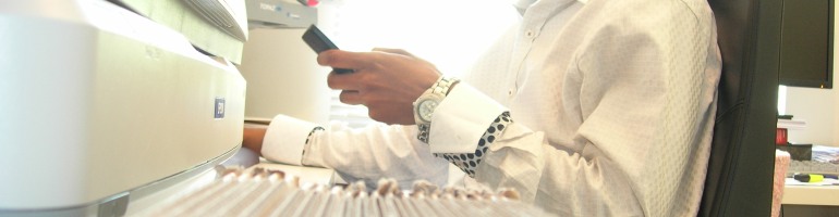 Image of a guy sitting on a chair in a brightly lit office with blinding light falling through the window, dressed in a white shirt, scrolling on his phone